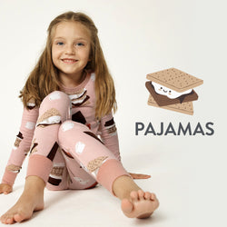 Child wearing pink pajamas with s'mores design, sitting on a white background.